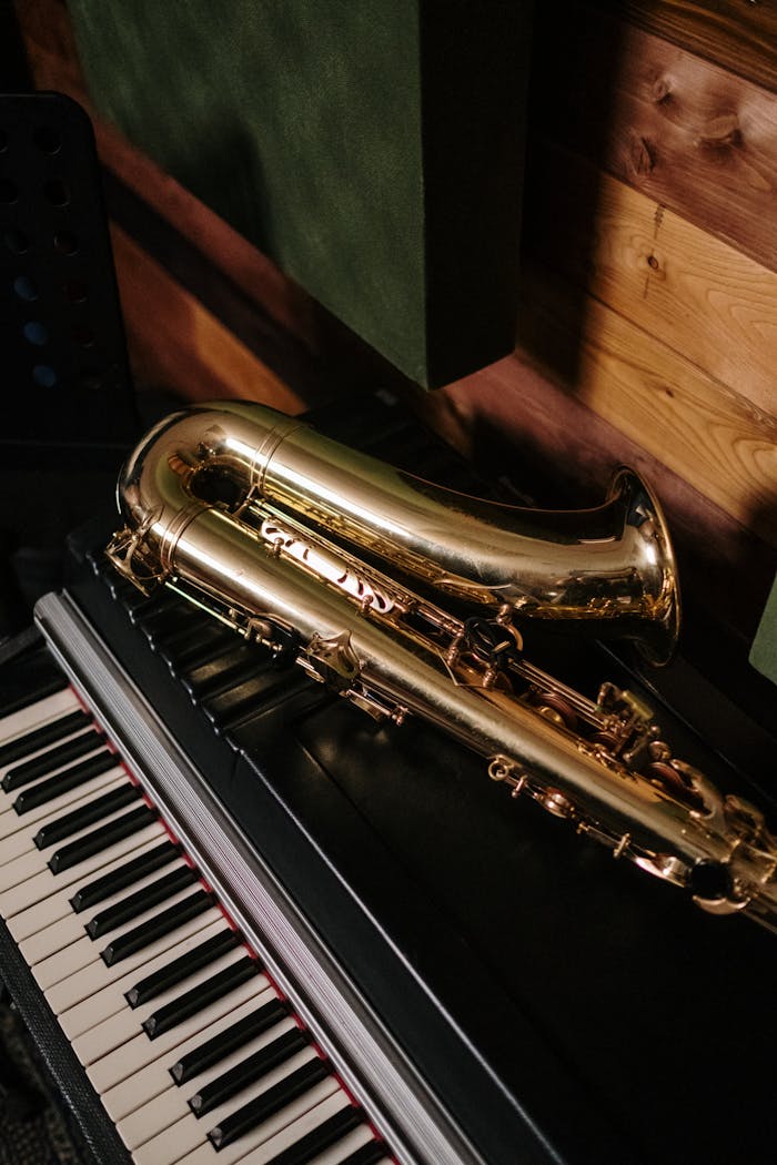 A gold saxophone resting on a black piano in a cozy, wooden music studio.